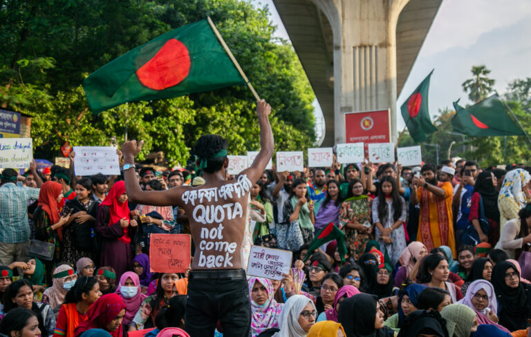 An image showing student protestors holding flags under a main overpass in Dhaka, Bangladesh.