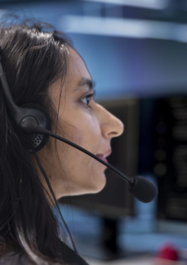 Admin in data center facility managing call center tasks, speaking into headset microphone while monitoring multiple PC screens. Indian woman talking with customers through headphones mic