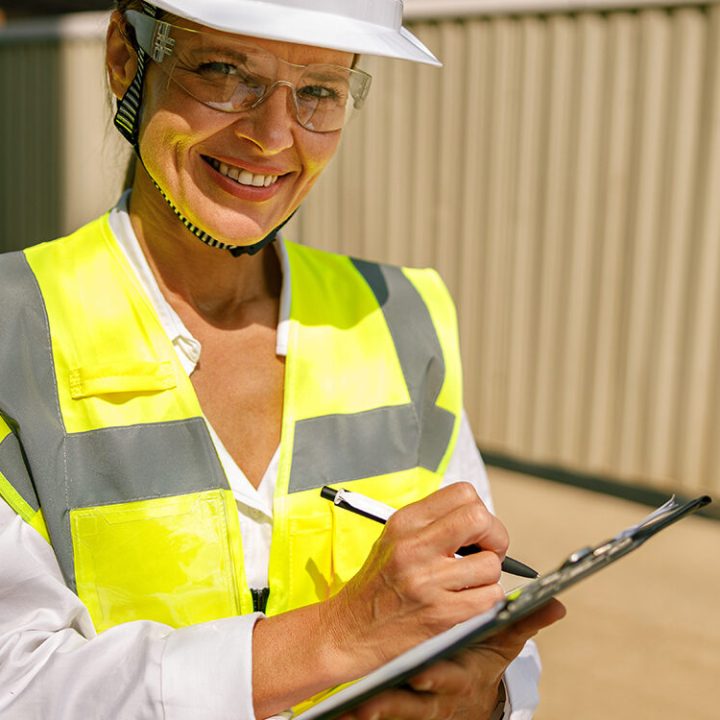 Professional female engineer in protective helmet making notes on construction site