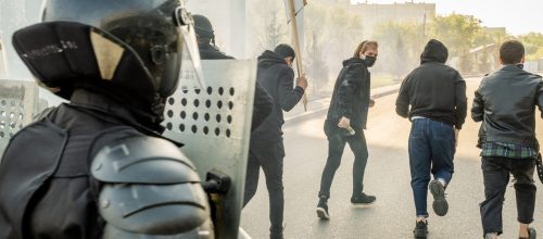 A policeman protecting himself a civilian protest, a risk that can affect businesses.
